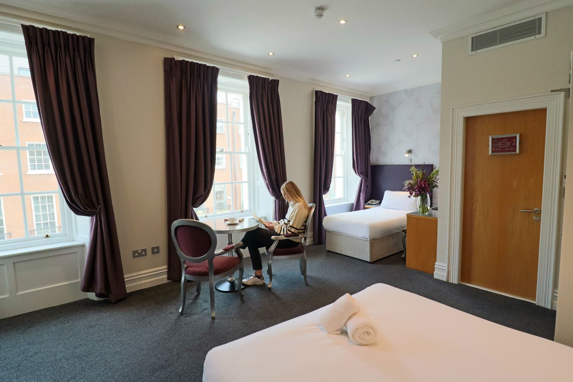 Wide view of the woman sitting at the table reading with a double bed and a king bed